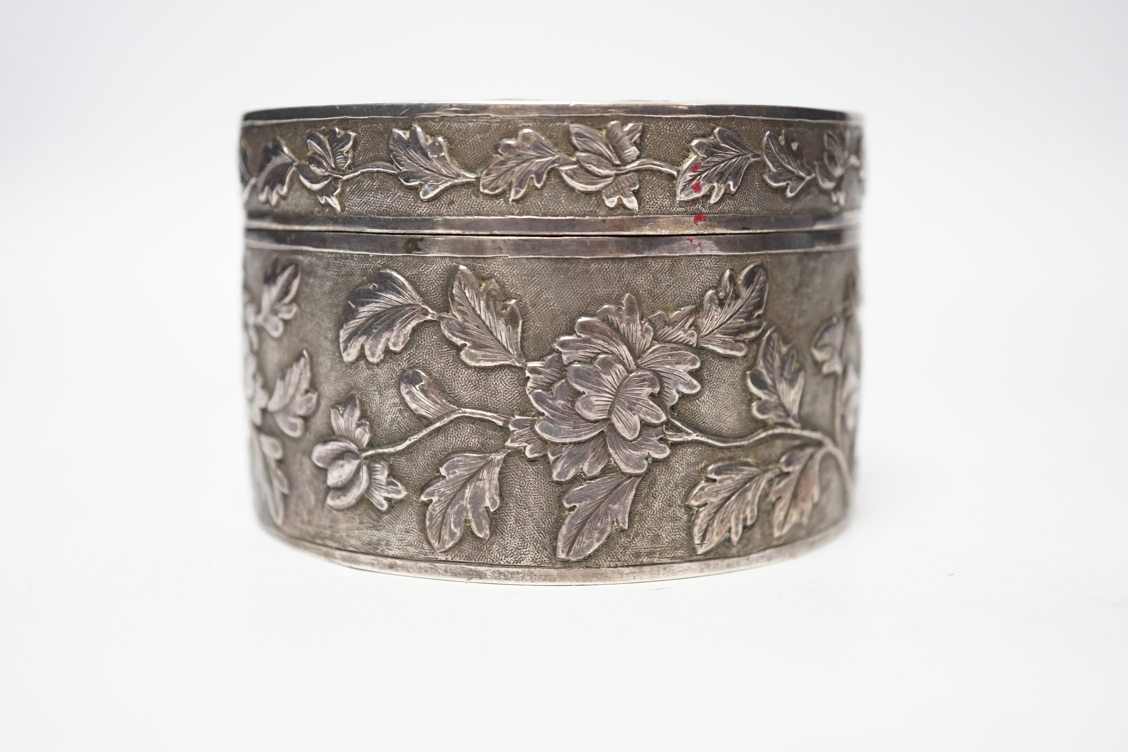 An early 20th century Chinese white metal circular box and cover, maker's mark MK, with foliate decoration and engraved inscription, diameter 82mm, 128 grams.